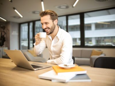 Business man smiling as he holds a mug and uses his laptop at his desk.