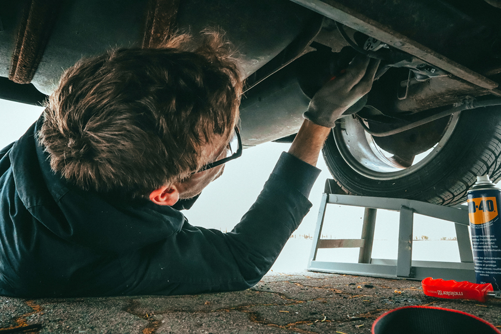 A mechanic works underneath a car at a car dealership.