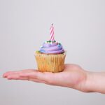 A person's hand with a cupcake with a birthday candle.