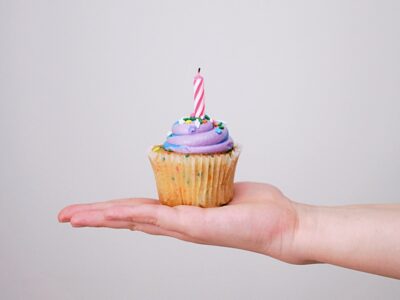 A person's hand with a cupcake with a birthday candle.