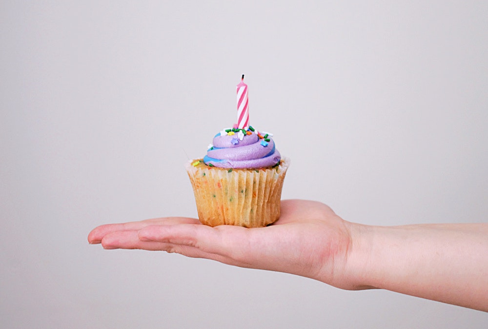 A person's hand with a cupcake with a birthday candle.