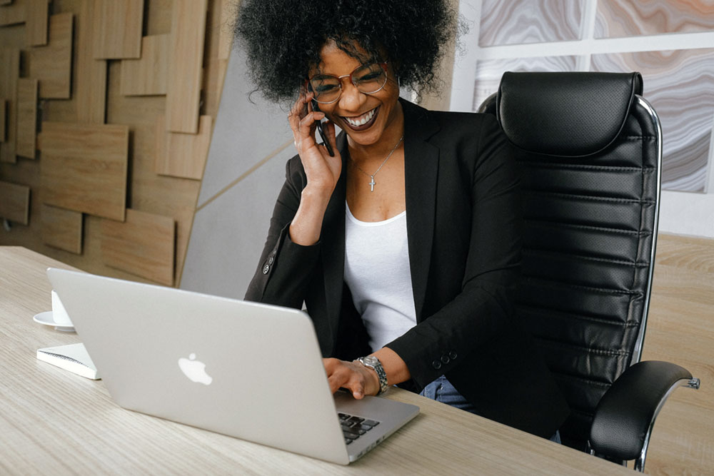 Young business woman smiling as she talks on her cell phone and works at her laptop.