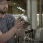 A man holding a part in a manufacturing facility.