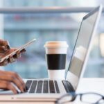 Woman working on laptop and phone.