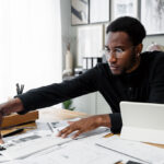 Man working at a desk with a tablet and multiple papers.