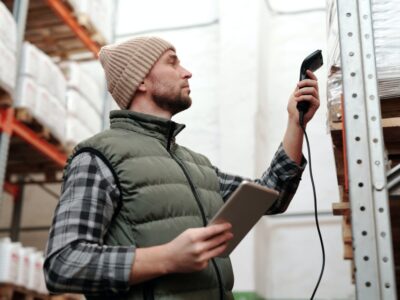 Man holding a tablet and scanning an item on a warehouse shelf.