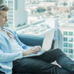 Young business man sitting on black sofa as he works on his laptop.