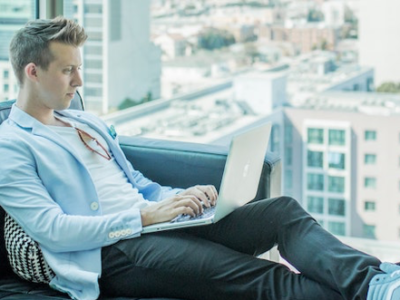 Young business man sitting on black sofa as he works on his laptop.