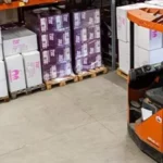 Fork lift in a warehouse with boxes on shelves in background.