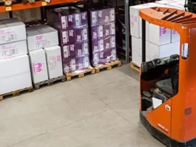 Fork lift in a warehouse with boxes on shelves in background.