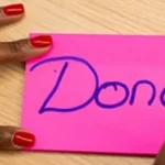 Woman with red nails writing "Done" on a pink note.