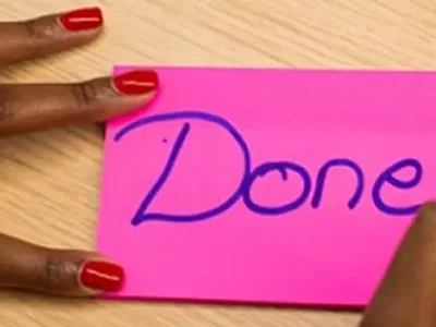 Woman with red nails writing "Done" on a pink note.