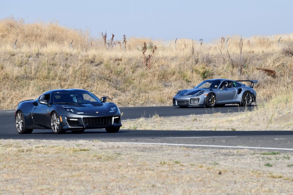 Two grey sport cars driving down a road in a rural setting.