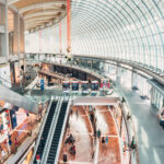 Inside view overlooking a large two story shopping mall with glass dome windows and escalators.