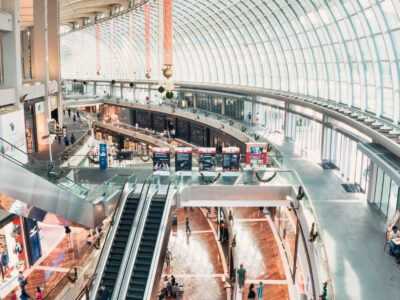 Inside view overlooking a large two story shopping mall with glass dome windows and escalators.