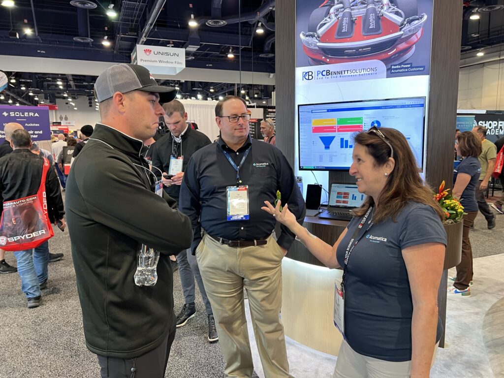 Scott McLaughlin meets PC Bennett's CEO Patricia Bennett and COO Tim O'Sullivan at SEMA 2023 in the Acumatica booth.