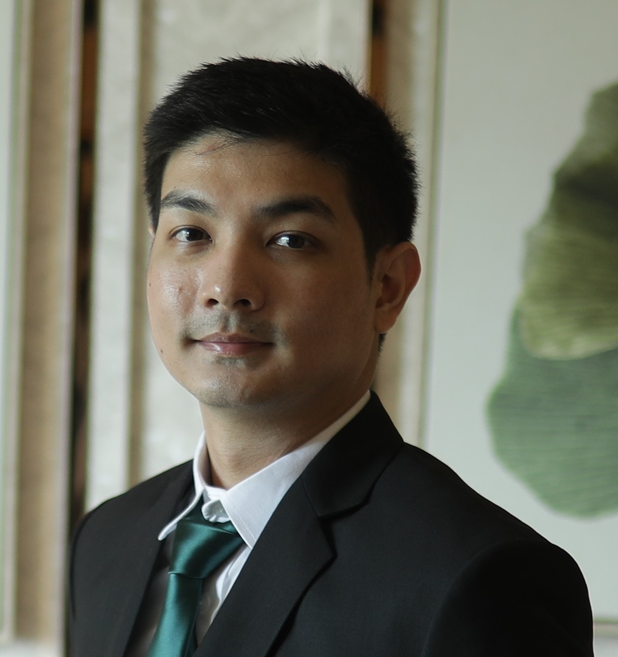 A man in a dark suit, white shirt, and green tie from the PC Bennett Solutions team looks at the camera with a neutral expression, standing indoors with abstract decor in the background.