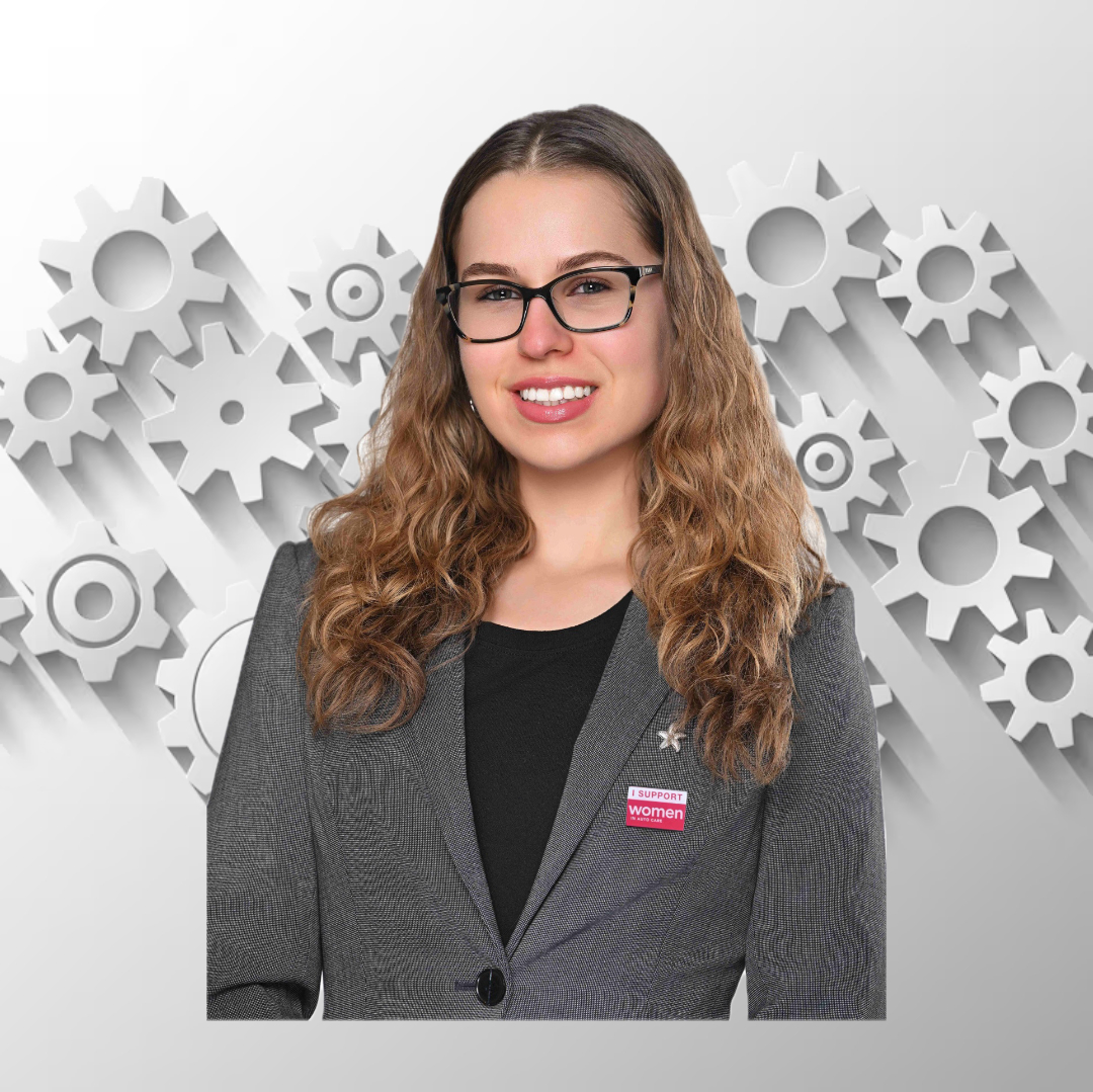 A woman with long curly hair and glasses, wearing a gray blazer with a "women" pin, stands smiling in front of floating white gears—proudly representing the PC Bennett Solutions team.